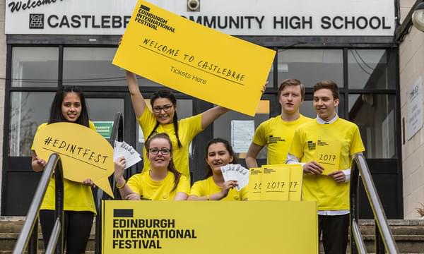 A group of high school students in yellow t-shirts smile holding signs with Edinburgh International Festival branding