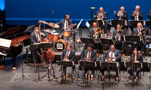 An orchestra play on stage, in front of a blue background