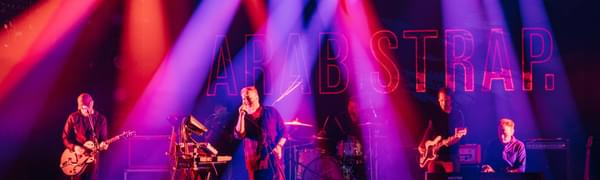 Arab Strap perform on stage under red, pink and purple spotlights
