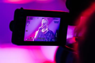 A shot of a video camera showing a man singing into a microphone