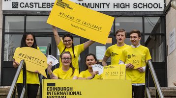 A group of high school students in yellow t-shirts smile holding signs with Edinburgh International Festival branding
