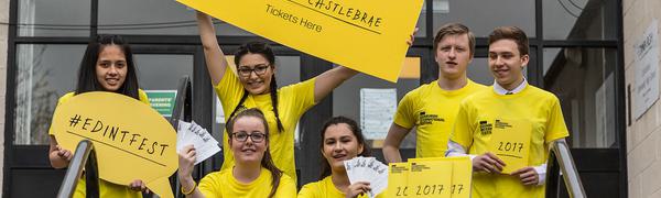 A group of high school students in yellow t-shirts smile holding signs with Edinburgh International Festival branding