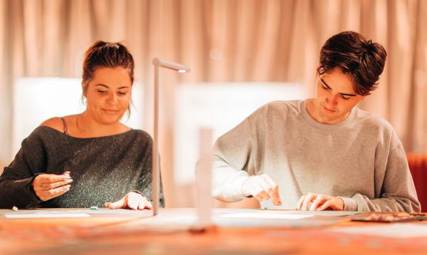 A man and a woman sit at a table drawing pictures with coloured crayons