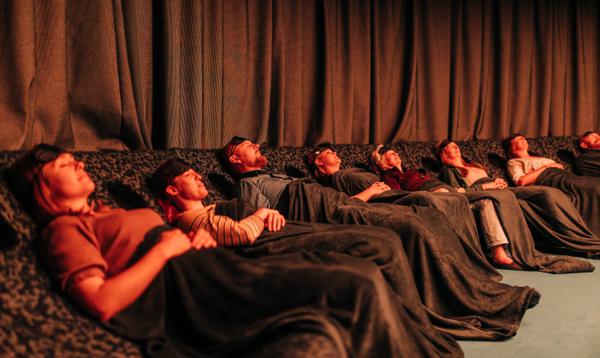 A group of people lie back under blankets with eye masks on their foreheads