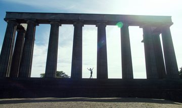 A male ballet dancer stands with arms outstretched between two columns on the National Monument of Scotland