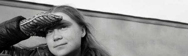 The activist pictured in black-and-white leaning against a wall, looking up and shielding her eyes with a mittened hand.