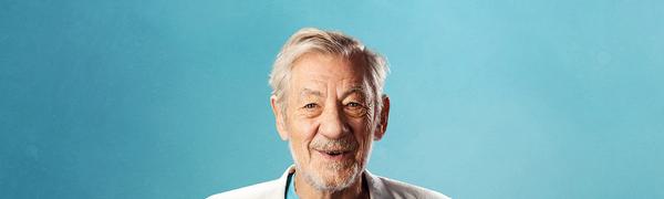 Sir Ian McKellan, pictured smiling at the camera wearing a turquoise t-shirt with a large '80' on the front and a white blazer