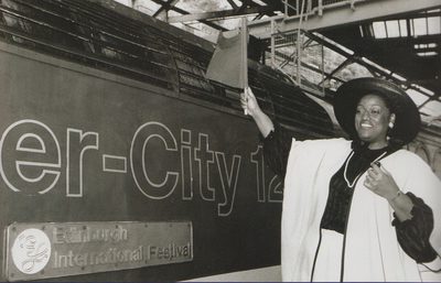 Jessye Norman stands on a train platform waving a flag