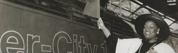 Jessye Norman stands on a train platform waving a flag