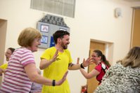A man in a yellow Festival t-shirt dances in the middle of a group of woman dancing around him.