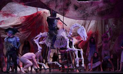 A man in armour holding a sword rides a skeletal horse