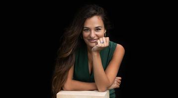 The violinist pictured wearing a green top, leaning forwards with her chin resting in her hand and smiling at the camera.