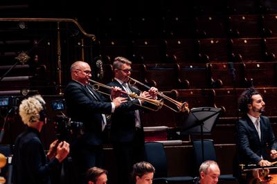 Two white men in black suits play old fashioned brass instruments