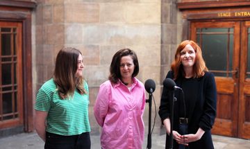 Three women stand in front of a microphone in the vestibule of Leith Theatre