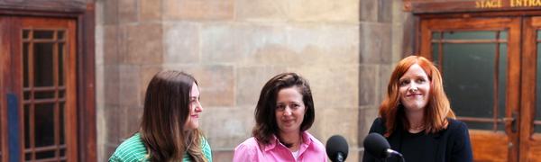 Three women stand in front of a microphone in the vestibule of Leith Theatre