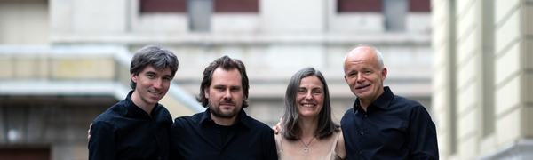 The quartet pictured standing with their arms around each other in a courtyard, smiling at the camera.