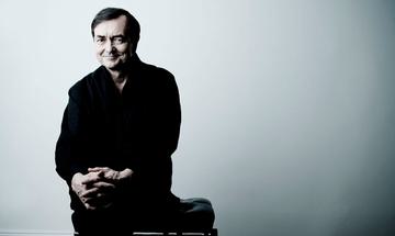 The pianist pictured seated on a piano stool smiling at the camera, wearing a black shirt and trousers.