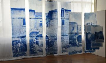 A hanging screen print of a brick farmhouse, printed in blue ink against several sheets of white fabric.