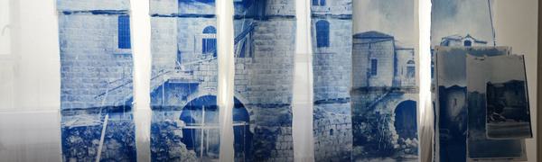 A hanging screen print of a brick farmhouse, printed in blue ink against several sheets of white fabric.