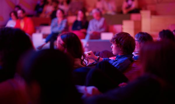 Young people sit watching a performance, the rest of the audience all around them.