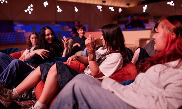 A group of teenagers sit on beanbags. Two of them pretend to play guitar.