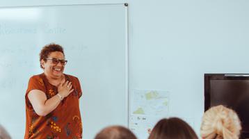 Jackie Kay stands smiling facing a group of seated people, with her hand over her heart.