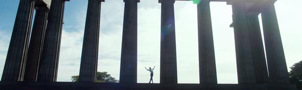 A male ballet dancer stands with arms outstretched between two columns on the National Monument of Scotland