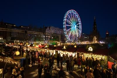 It is night time and there are bustling Christmas markets which are lit up below. A ferris wheel is illuminated on the skyline