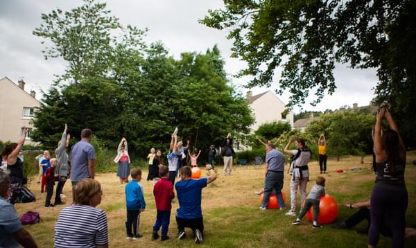 A group of families in a park shown with exercise balls following along a workshop