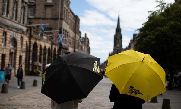 A view of an Edinburgh street with two Edinburgh International Festival umbrellas in the foreground, one yellow, one black.