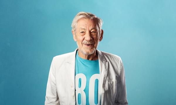 Sir Ian McKellan, pictured smiling at the camera wearing a turquoise t-shirt with a large '80' on the front and a white blazer