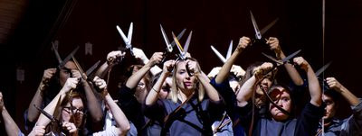 A group of women in Blue pinafores against a black background holding scissors