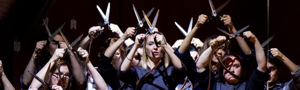 A group of women in Blue pinafores against a black background holding scissors