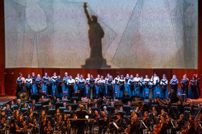 Statue of Liberty outline with a group of performers singing accompanied by an orchestra,