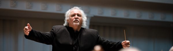 A man is standing in front of an orchestra, conducting