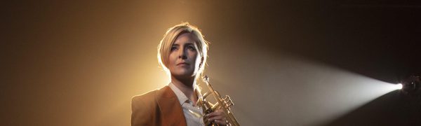 Woman standing holding wind instrument looking off camera, side lit by spotlight