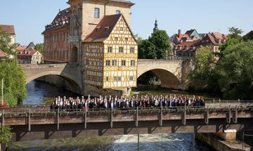 Large group of people standing together on bridge over river