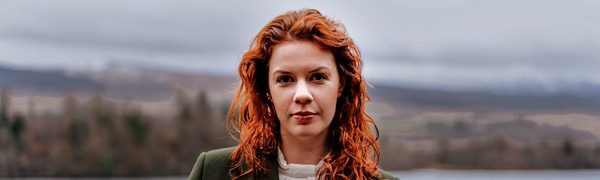 Woman with red hair standing by water facing camera