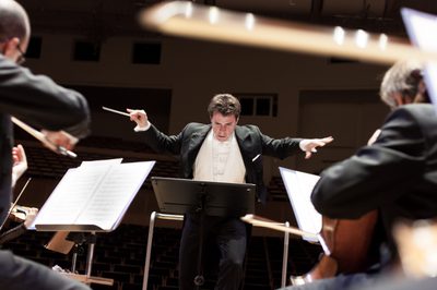 Man conducting orchestra with arms outstretched, looking down