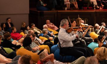 A group of people sitting on beanbags surround people playing the violin