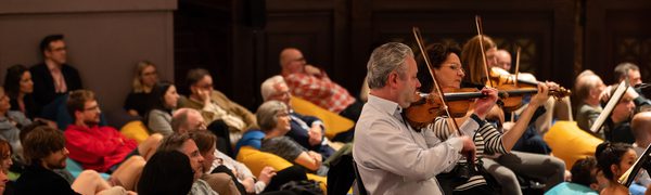 A group of people sitting on beanbags surround people playing the violin
