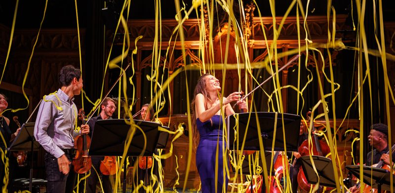 Yellow streamers descend from the ceiling on Nicola Benedetti and a group of musicians.
