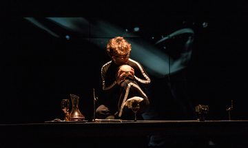 Man crouched on stage holding skull