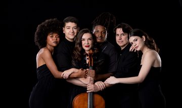 Woman holds stringed instrument people gathered around her with arms entwined