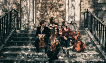 Four women sitting on stairs in dappled light, holding stringed instruments looking right
