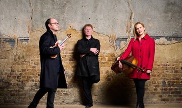 Man leaning on wall, man and woman either side holding stringed instruments