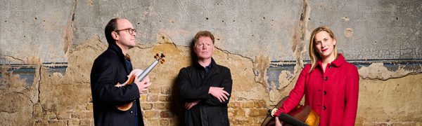 Man leaning on wall, man and woman either side holding stringed instruments