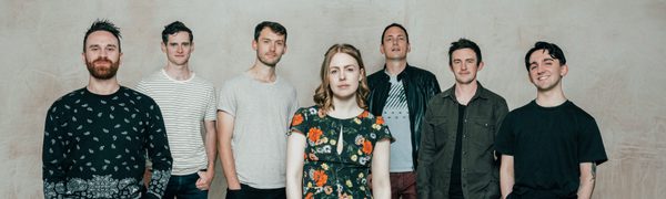 Woman Standing in front of six men all facing camera and smiling