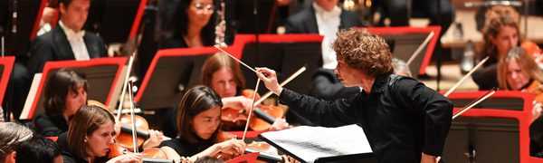 Man Arms outstretched towards stringed musicians, conducting orchestra performance