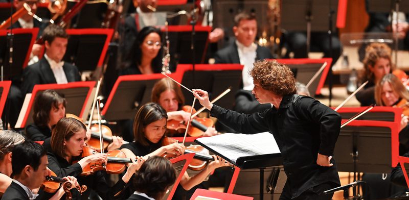 Man Arms outstretched towards stringed musicians, conducting orchestra performance